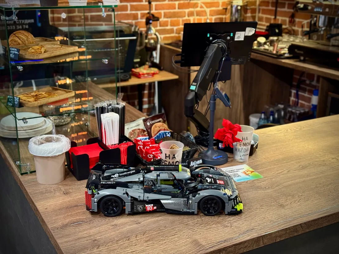 Модель гоночного Peugeot на кофейной стойке KarCoffe рядом с витриной выпечки