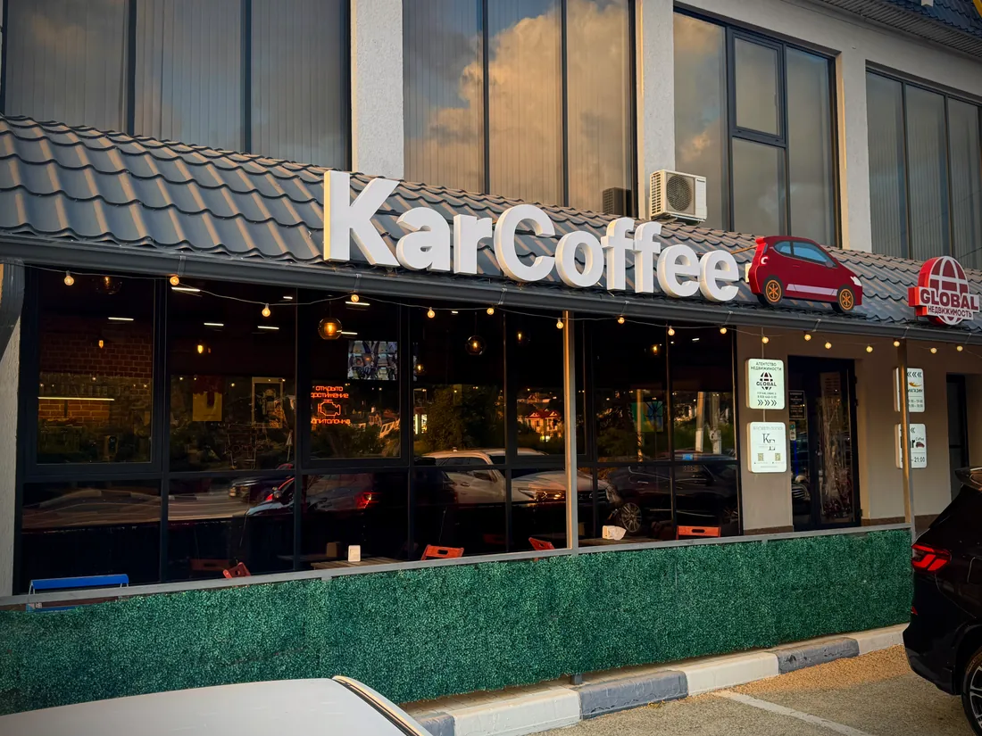 Фасад кафе KarCoffe с вывеской и красным автомобилем в вечернем свете